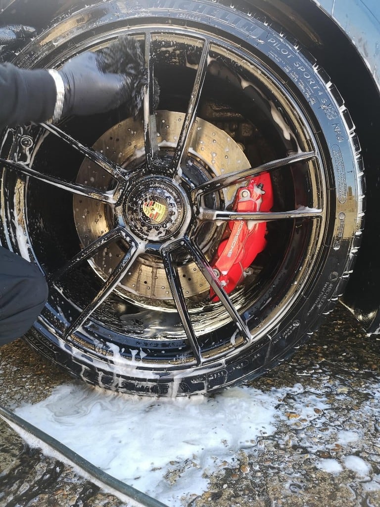 Porsche alloy wheel and red brake caliper being deep-cleaned