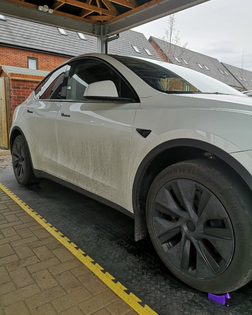 White Tesla Model Y with road grime down the side before cleaning